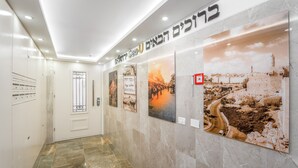 Un couloir au sol et aux murs recouverts de marbre, avec une porte dotée d’un portail en métal, un interrupteur fixé au mur et une affiche avec du texte en hébreu.