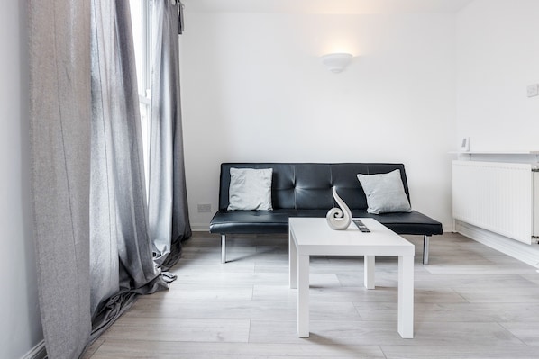 A modern living room with a black leather sofa, white cushions, a white coffee table, and a grey curtain.