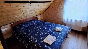 Huoneessa on puinen, kalteva kattopinta, tähtiä kuvaavalla kuviolla koristeltu peitto sängyllä ja valkoinen verho ikkunassa.