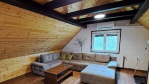Tunnelmallinen, avoimen pohjaratkaisun huone, jossa on puinen kattopalkisto, kulmasohva, sohvapöytä ja suuri ikkuna.