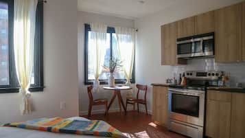 Quarto com cama, mesa de cabeceira, janela com cortinas e vista para um edifício.