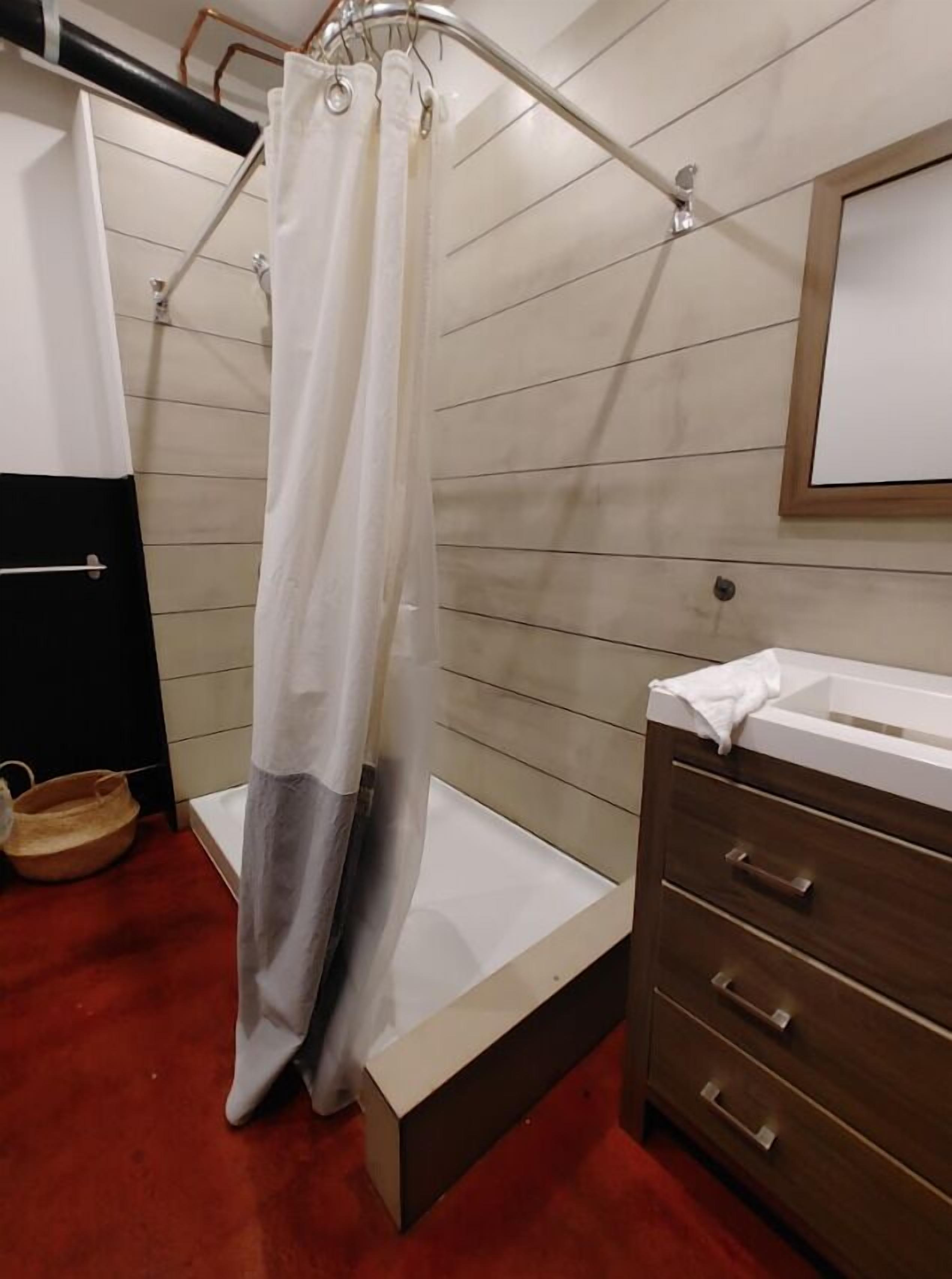 A bathroom with a shower curtain, a bathtub, a wooden vanity with drawers, and a mirror.