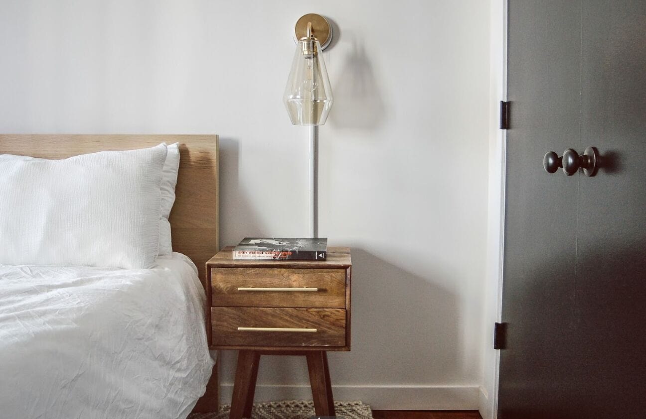 Quarto com cabeceira de madeira, mesa de cabeceira com abajur e uma porta.