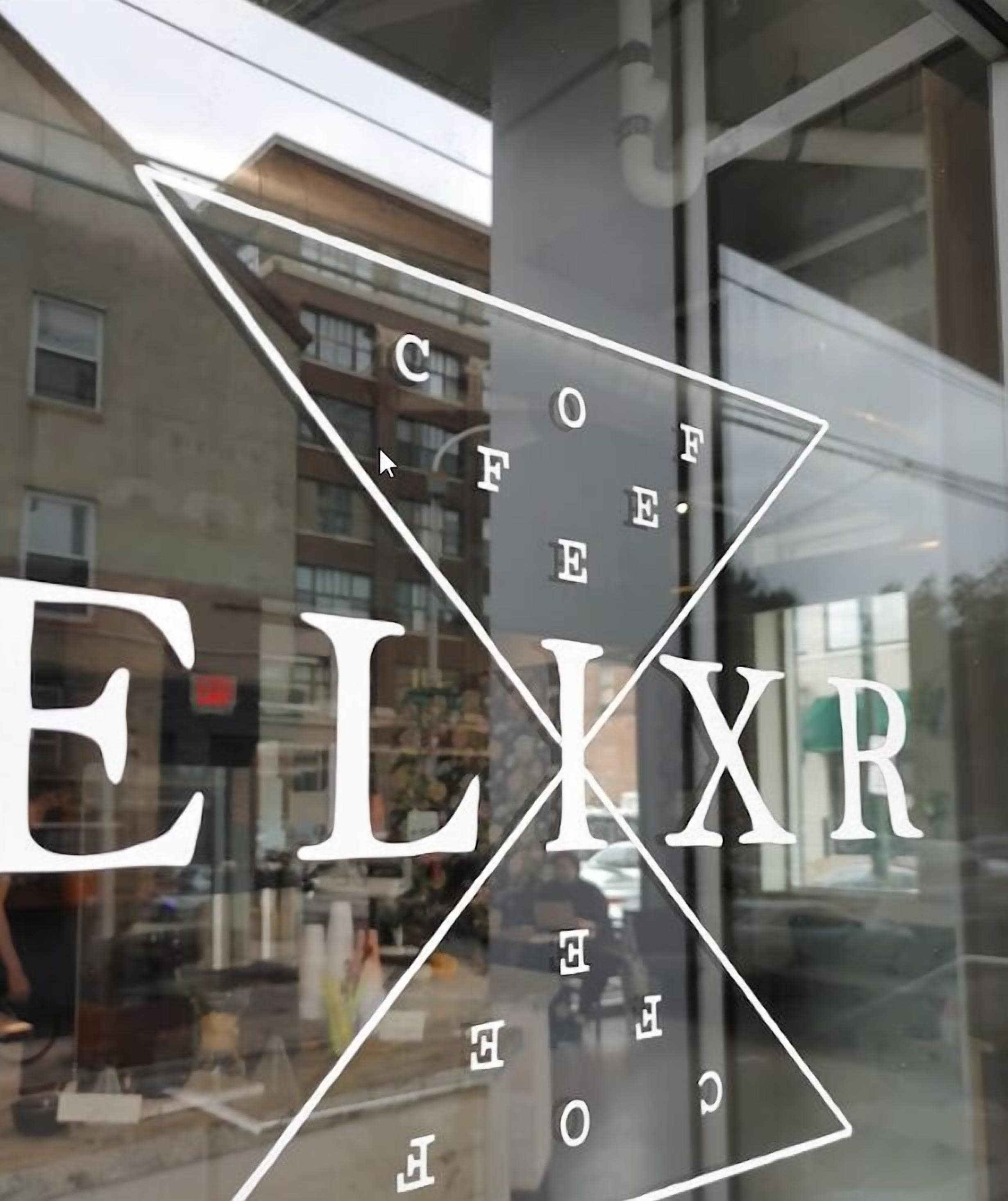 Une vitrine portant le nom « ELIXR » en grandes lettres, dans laquelle se reflètent un immeuble et une scène de rue.
