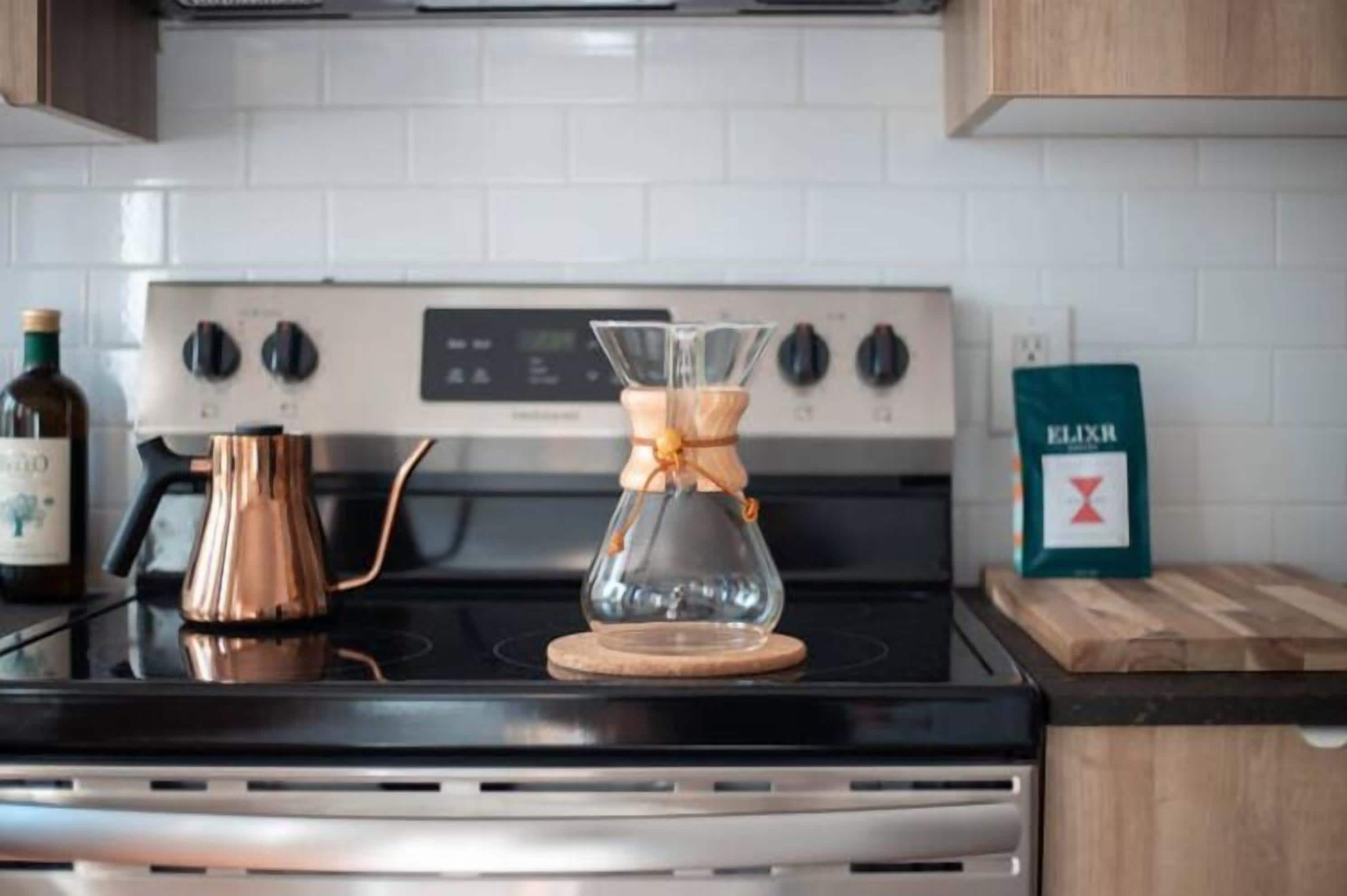 A kitchen with a stove, a glass carafe, and a coffee maker.