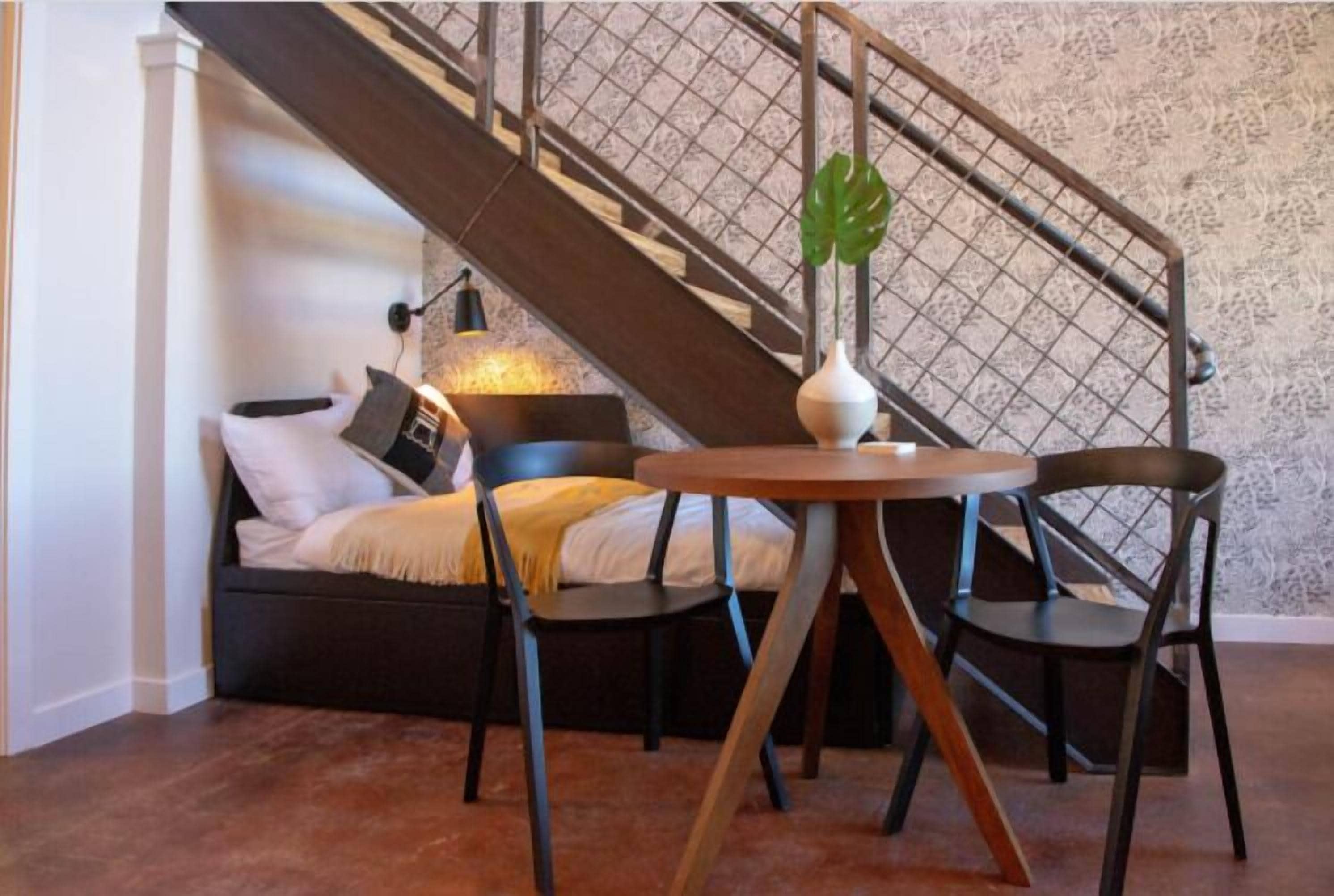 Une pièce confortable avec un lit, deux chaises, une petite table et un escalier doté d’une rampe en métal.