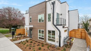 Et moderne hus i to etager med træfacade, en lille forhave med beplantning og en synlig garageport.