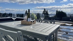 Et bord med to vinglas og en flaske på en tagterrasse med udsigt over byen.