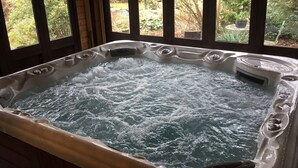 A hot tub with a view of a garden through wooden-framed windows.