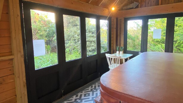 A wooden interior with a high ceiling, large windows, a bar area, and a patterned rug.