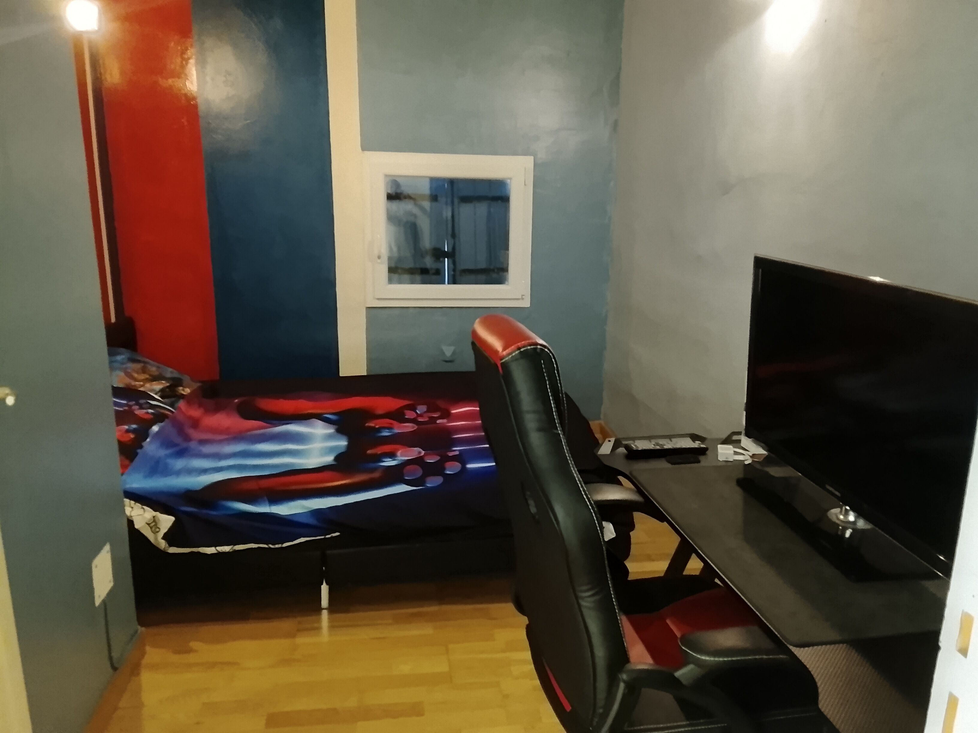 Una habitació petita amb un llit, un escriptori, una cadira i una televisió.