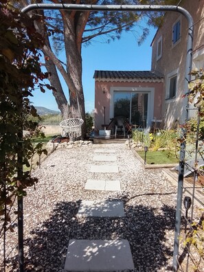 Un sentiero conduce a un edificio con tetto in tegole, un grande albero e un giardino con un canestro da basket.