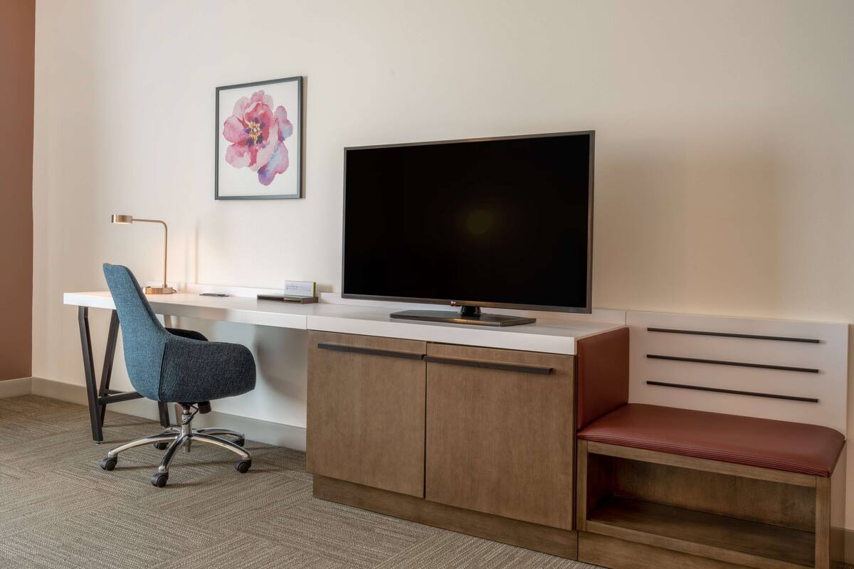 Een moderne hotelkamer met een bureau, stoel, televisie en een bankje.