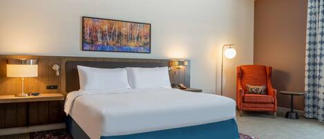 Una habitación de hotel con cama, mesita de noche, lámpara, silla y un cuadro en la pared.