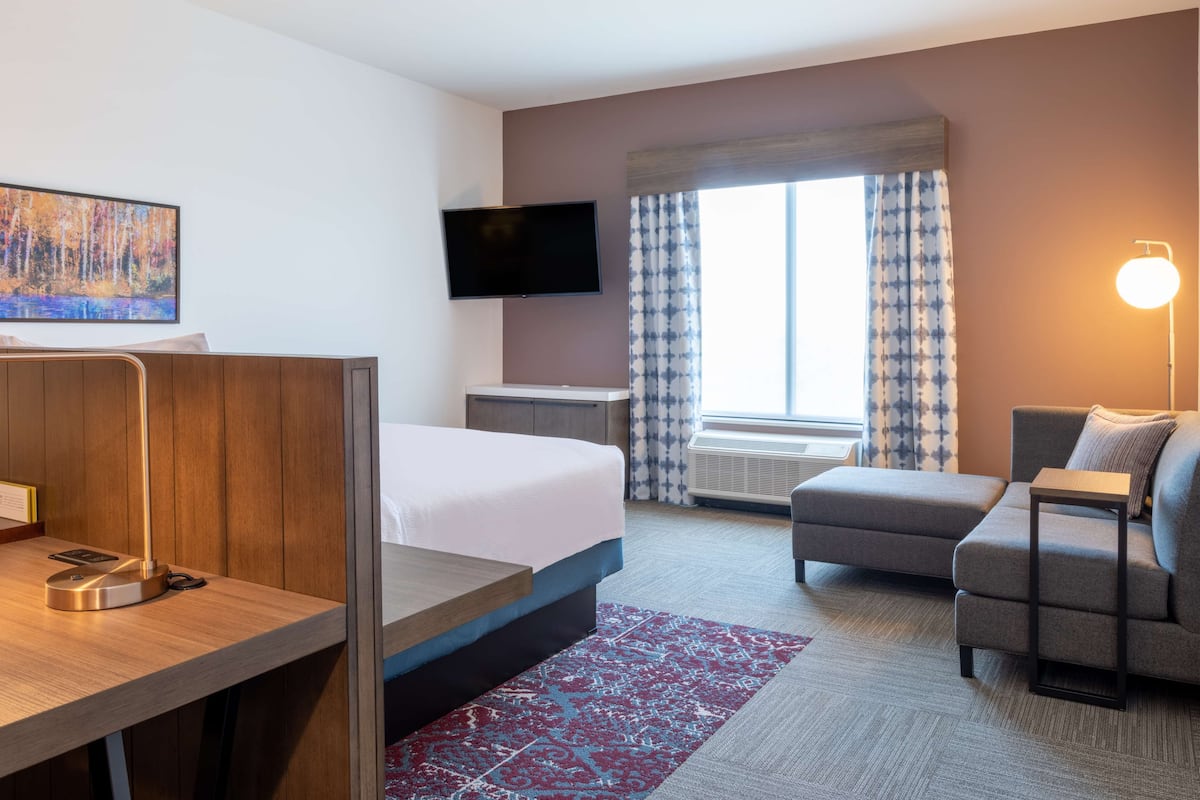 Hotelkamer met een bed, bureau, bank, televisie en raam met gordijnen.