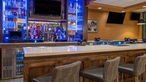 Un espace bar comprenant un comptoir, des tabourets de bar, un téléviseur et des étagères remplies de bouteilles d’alcool et de verres.