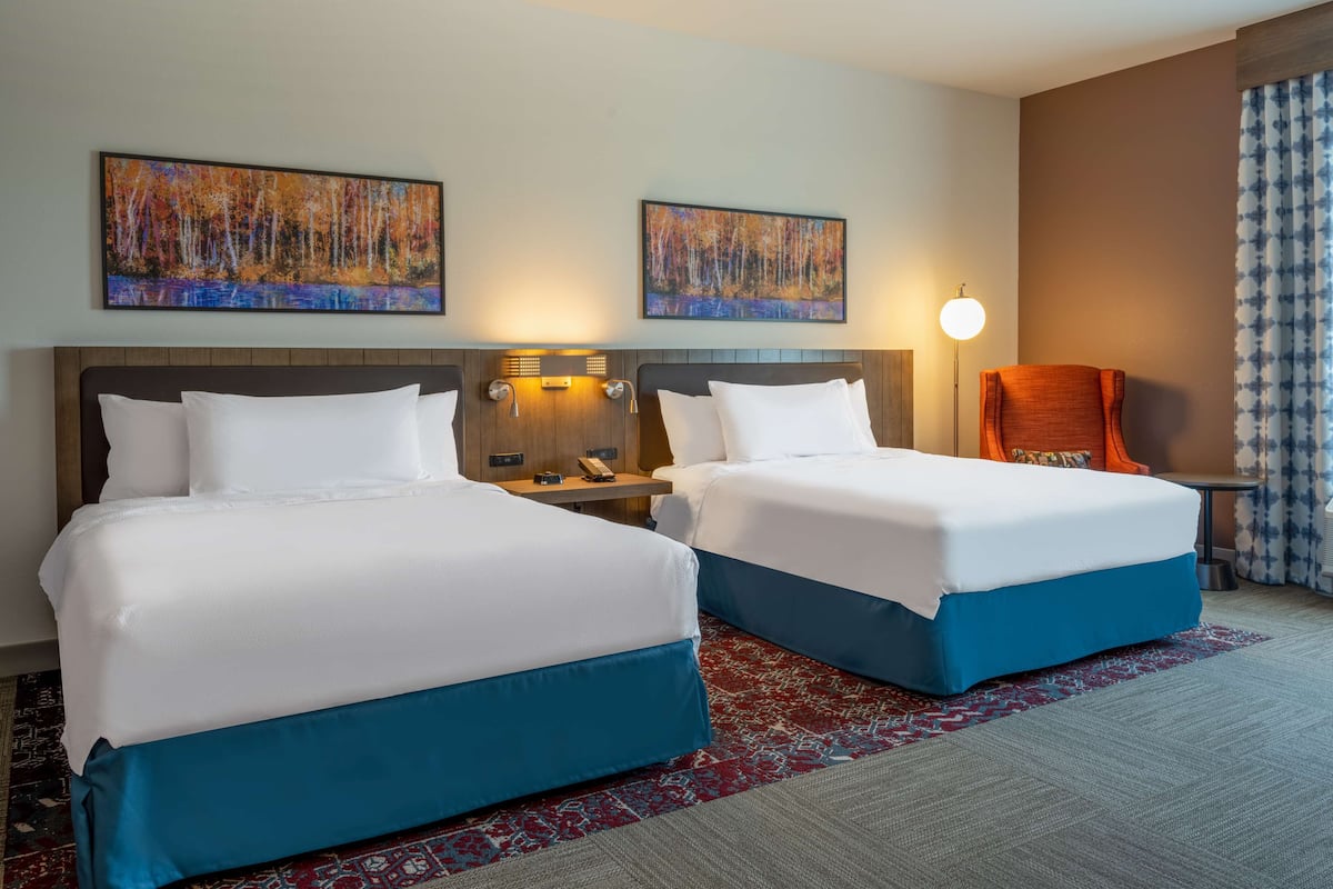 Een hotelkamer met twee bedden, een nachtkastje met een lamp en een stoel.