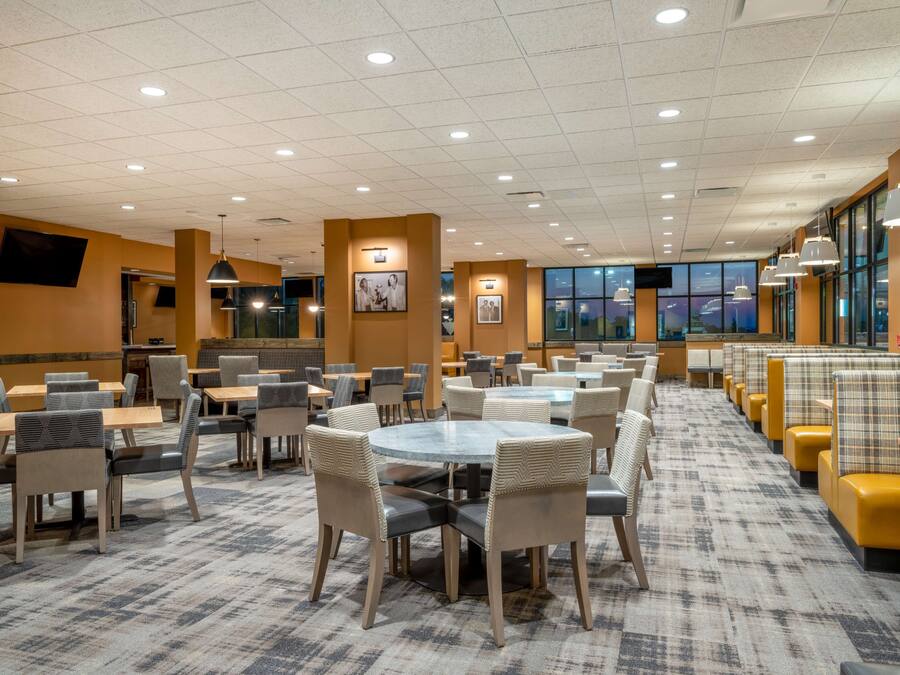 A spacious restaurant with multiple seating areas, including round tables and booths, and a carpeted floor.