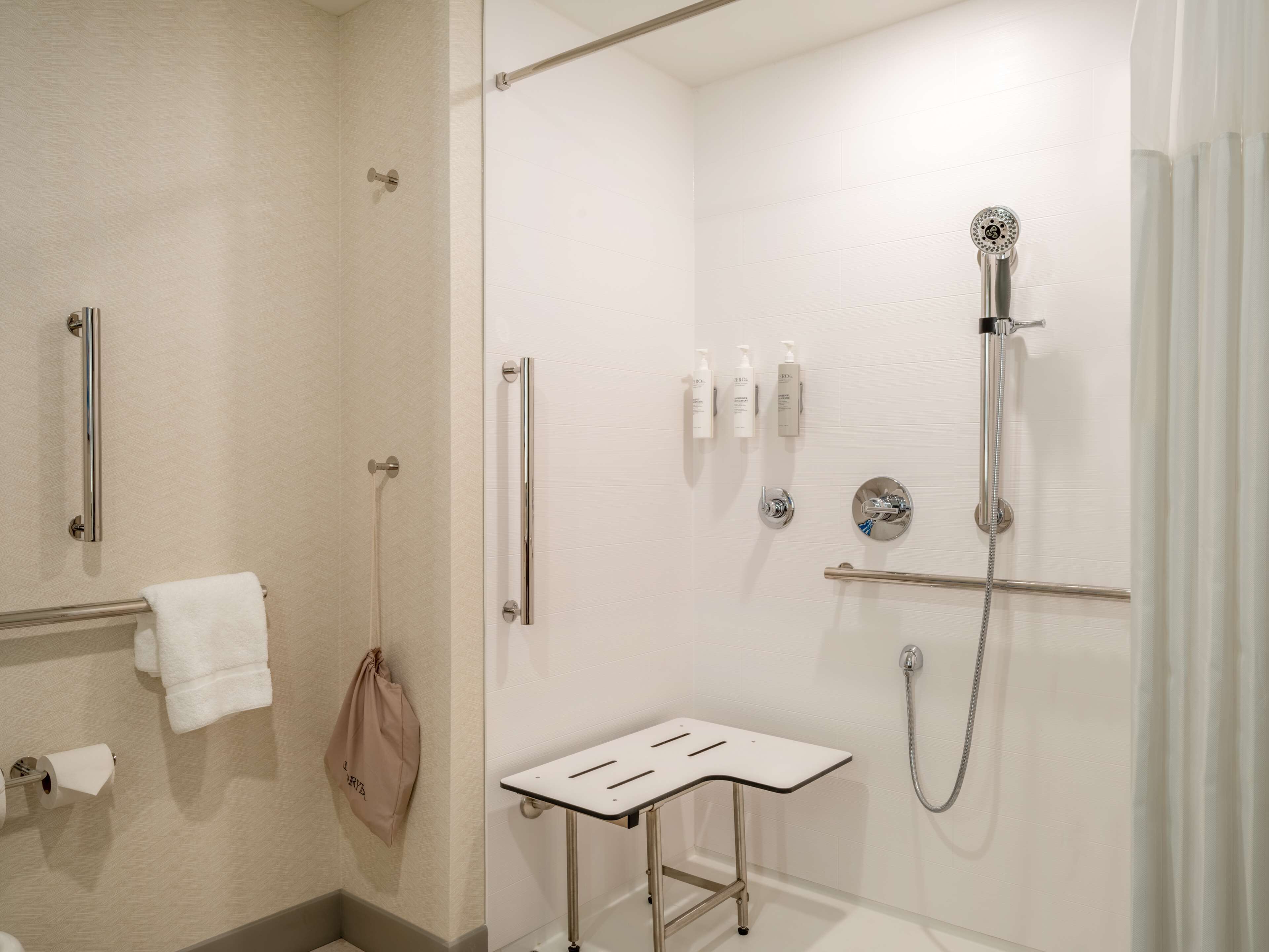 Un baño moderno con cabina de ducha de vidrio, un cabezal de ducha manual, un perchero y una mesita.