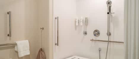 Un baño moderno con cabina de ducha de vidrio, un cabezal de ducha manual, un perchero y una mesita.