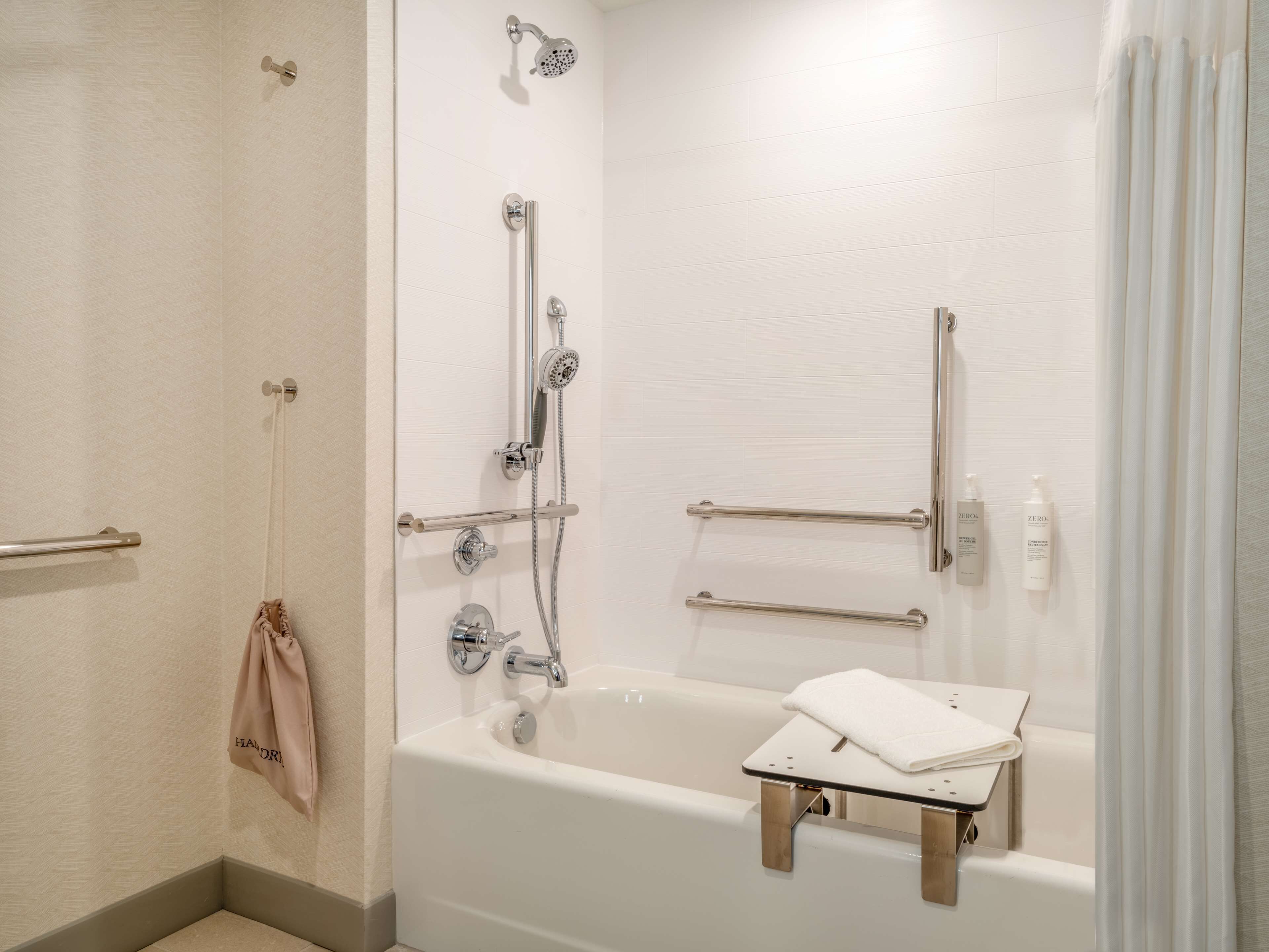 A modern bathroom with a bathtub, shower, and handrails.