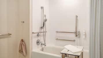 A modern bathroom with a bathtub, shower, and handrails.