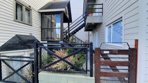 A residential building with a black metal gate, a wooden staircase, and a balcony with a potted plant.