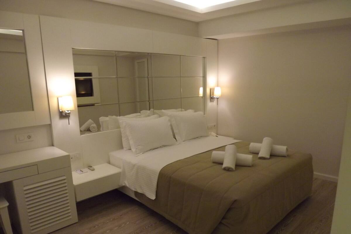 Une chambre d’hôtel moderne avec un grand lit, des tables de chevet, un bureau et un miroir.