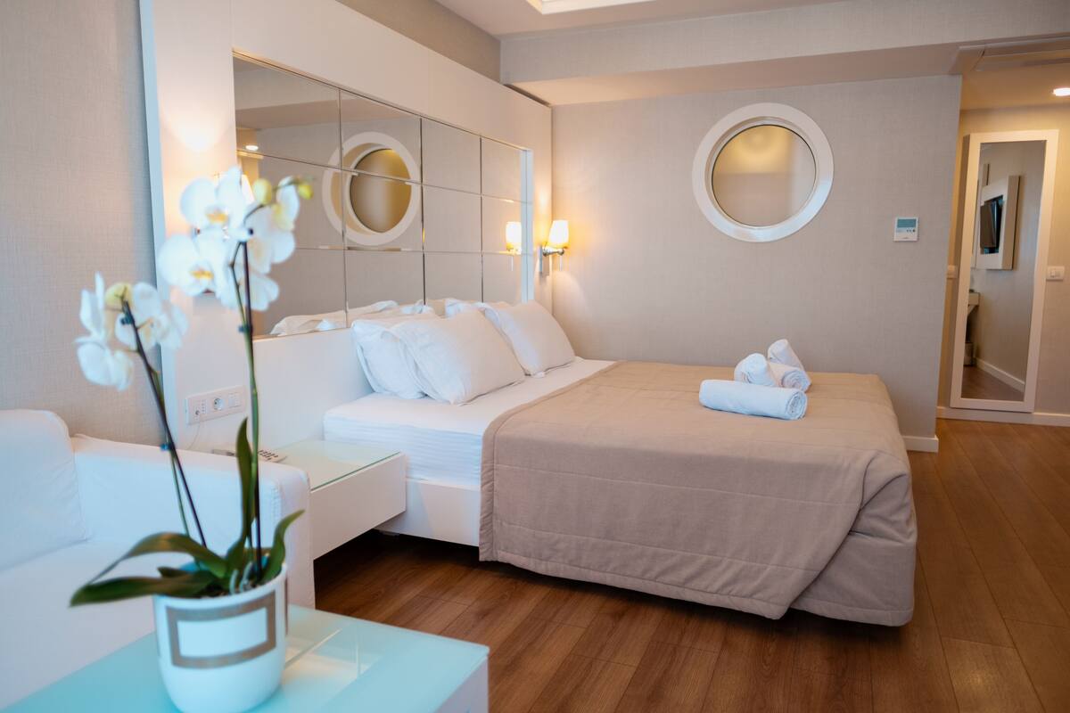 Une chambre d’hôtel avec un lit, une table de chevet, un miroir et une orchidée en pot.