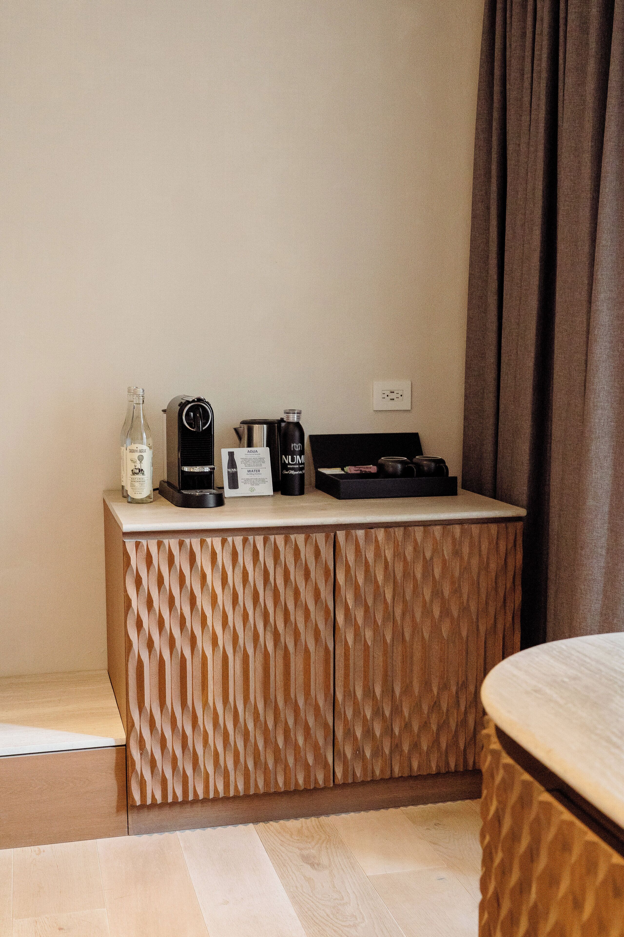 Una habitación de hotel con un mueble de madera que contiene una botella, una cafetera y un juego de té.