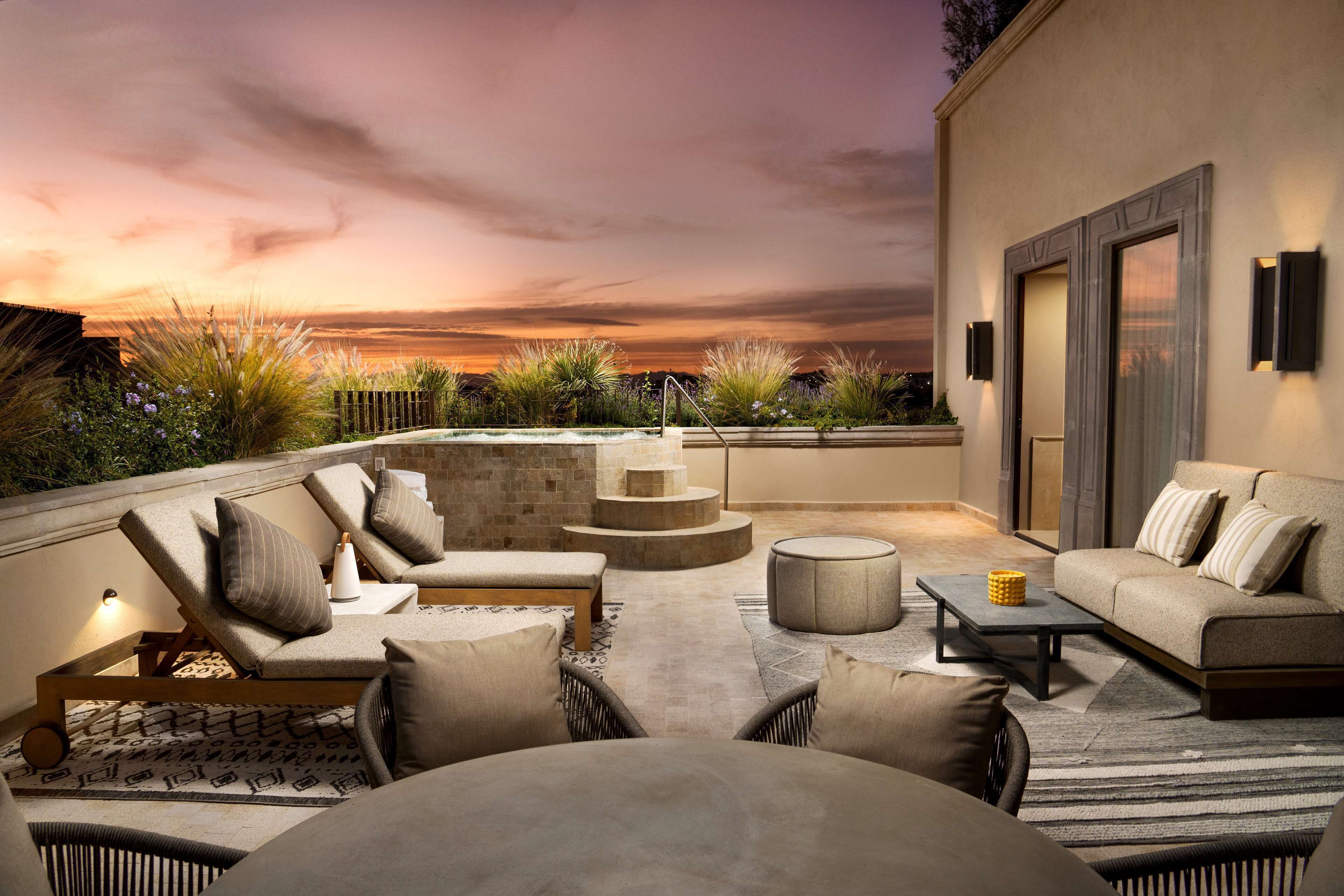 A rooftop lounge with outdoor seating, a fire pit, and a view of the sunset.