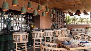 A bar area with wooden chairs and tables, hanging green pendant lights, and shelves with bottles and glasses. - NUMU Boutique Hotel, The Unbound Collection by Hyatt (San Miguel de Allende)