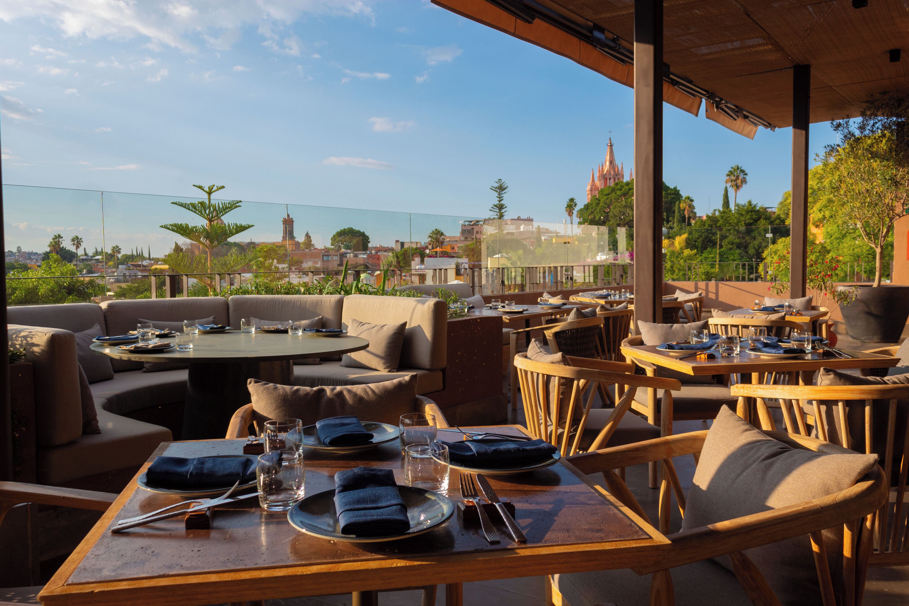 An outdoor dining area with tables and chairs, a view of a cityscape, and a building with a spire in the background.