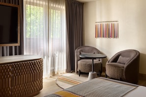 A hotel room with a large flat-screen TV, two armchairs, a small round table, and a patterned rug.