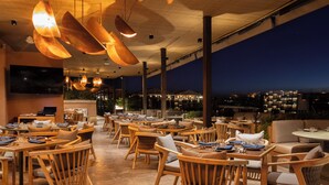 An outdoor dining area with wooden furniture and hanging lights, overlooking a cityscape at night. - NUMU Boutique Hotel, The Unbound Collection by Hyatt (San Miguel de Allende)