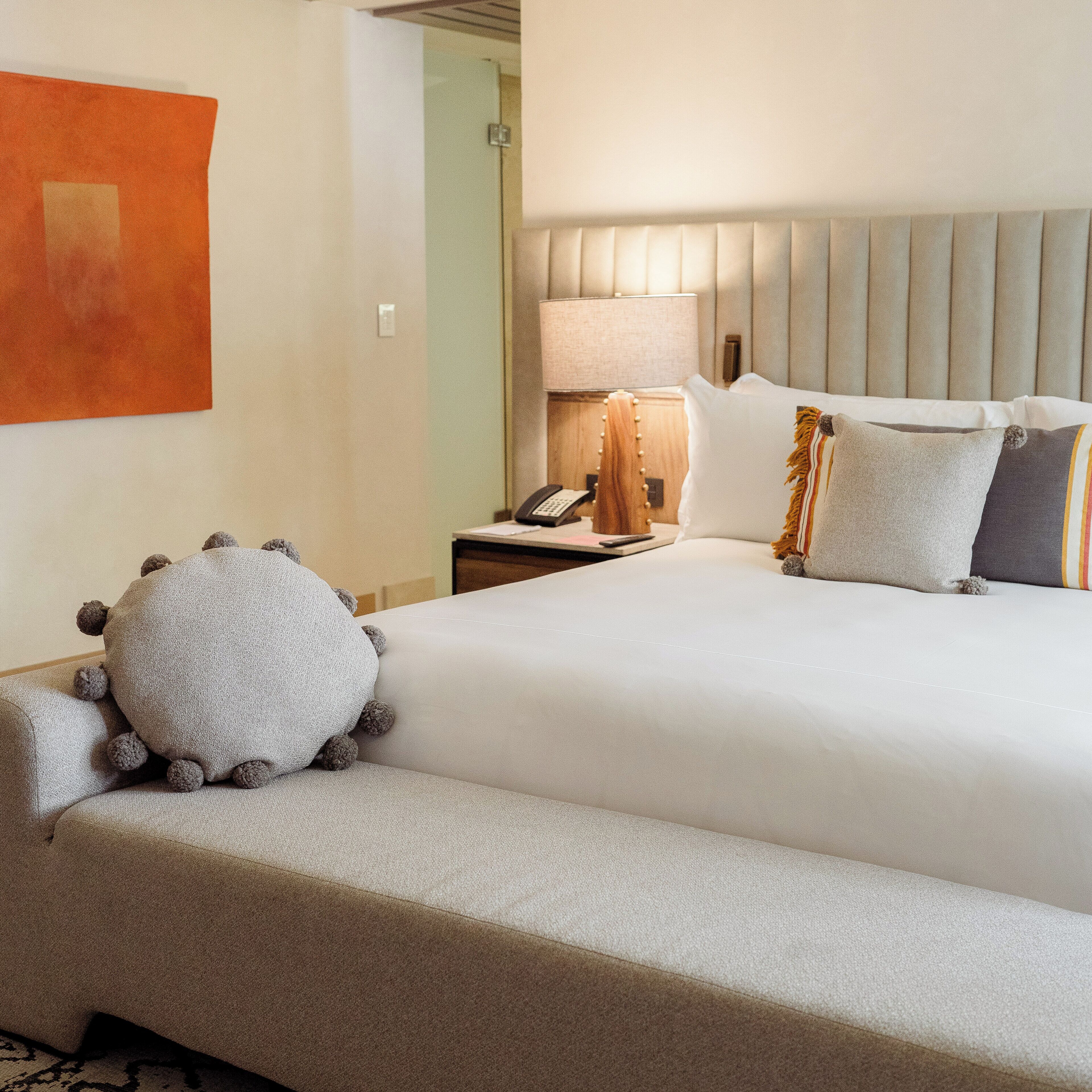 A hotel room with a large bed, a bedside table with a lamp, a telephone, and a decorative pillow.
