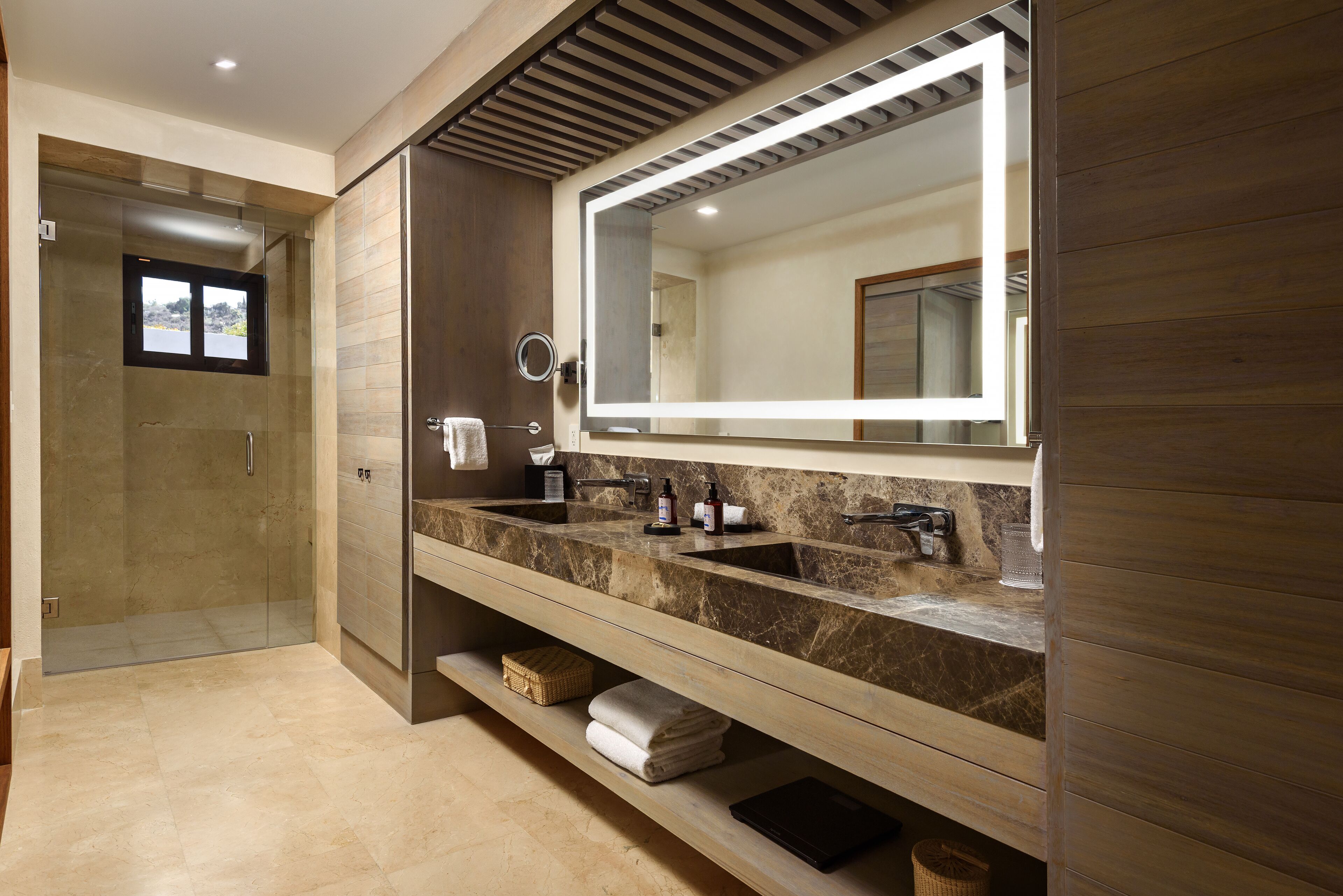 A modern bathroom with a large mirror, dual sinks, and a walk-in shower.
