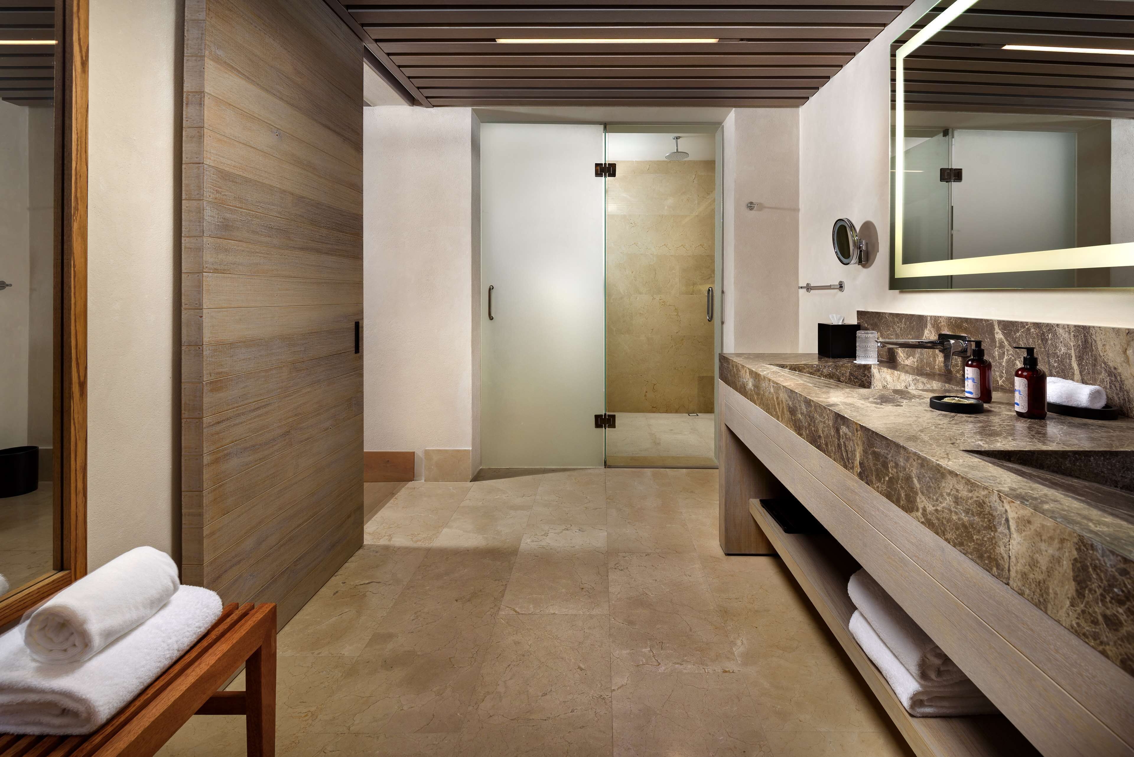 A modern bathroom with a wooden vanity, a large mirror, and a glass shower enclosure.