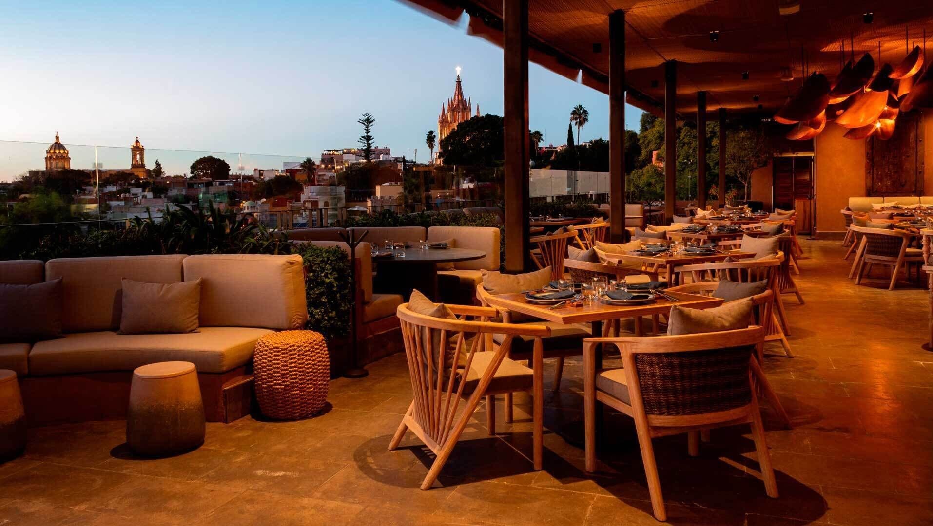 An outdoor dining area with tables and chairs, a sofa, and a view of a cathedral in the background.