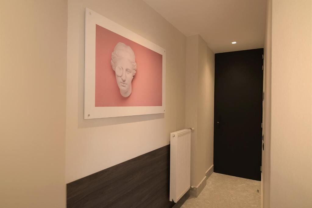 A hallway with a white-framed artwork on the wall, a radiator, and a dark door at the end.
