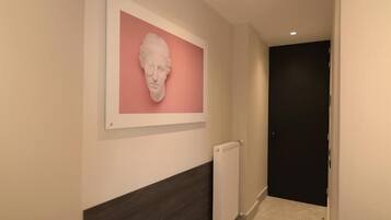 A hallway with a white-framed artwork on the wall, a radiator, and a dark door at the end.