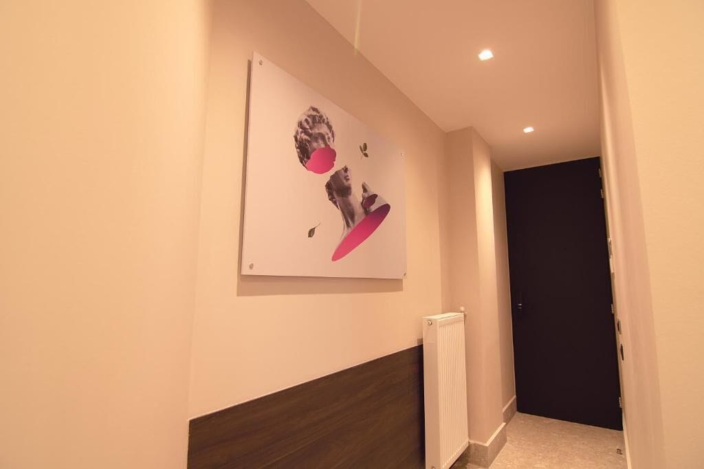 A hallway with a modern art piece on the wall, a radiator, and a dark door at the end.