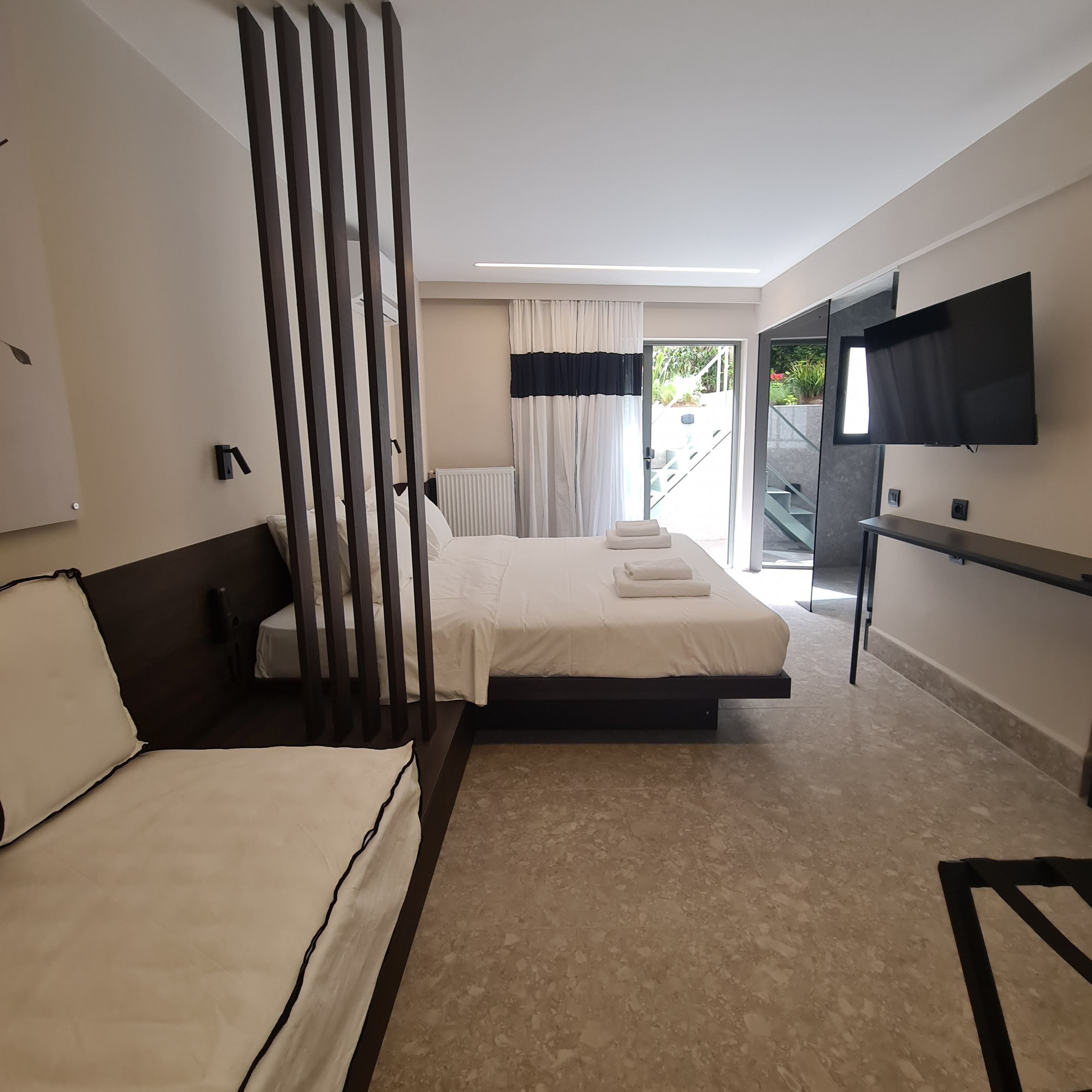 A modern hotel room with a large bed, a smaller bed, a TV, and a view of the outdoors.
