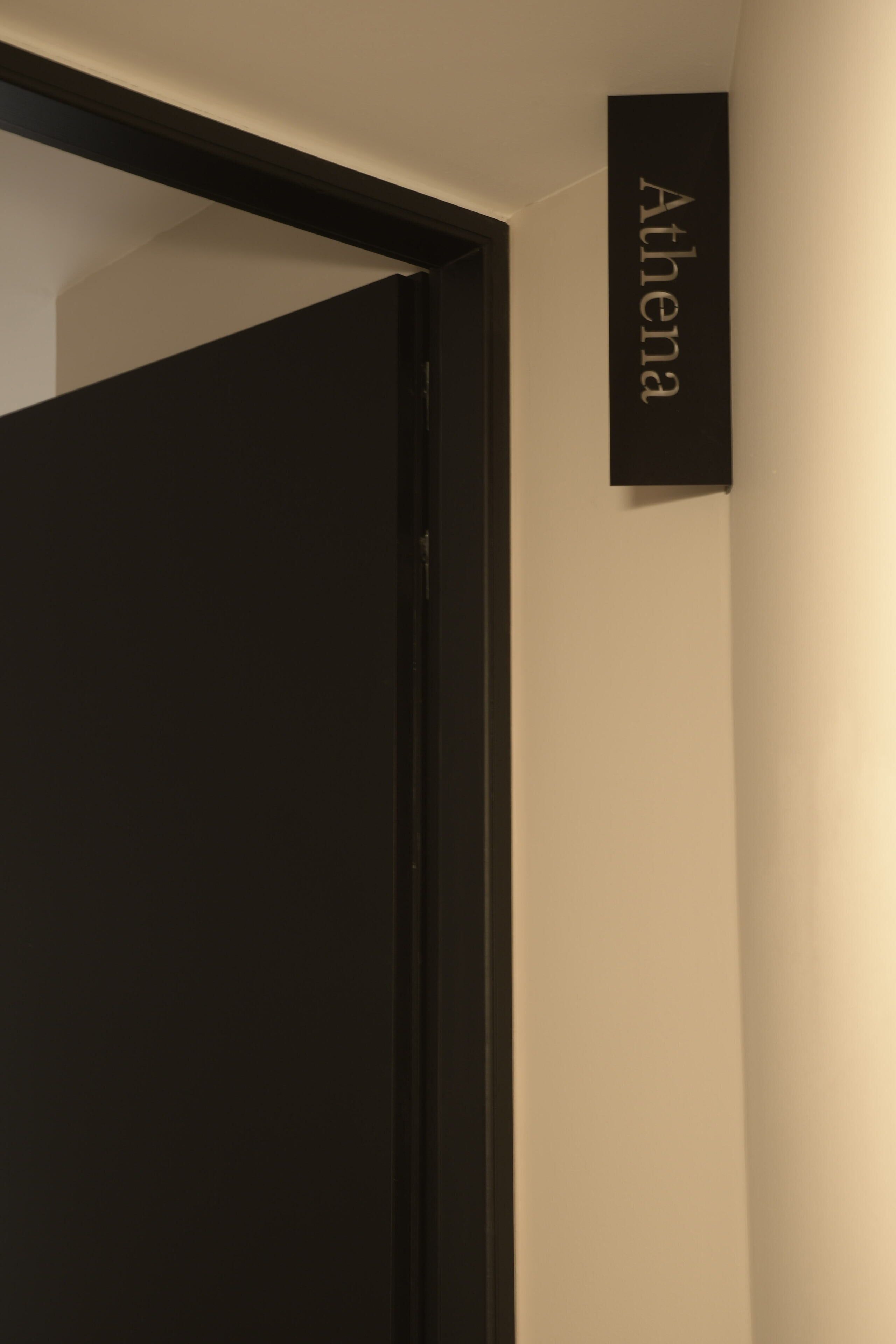 Un couloir avec une porte noire et une pancarte sur laquelle on peut lire « Athéna ».