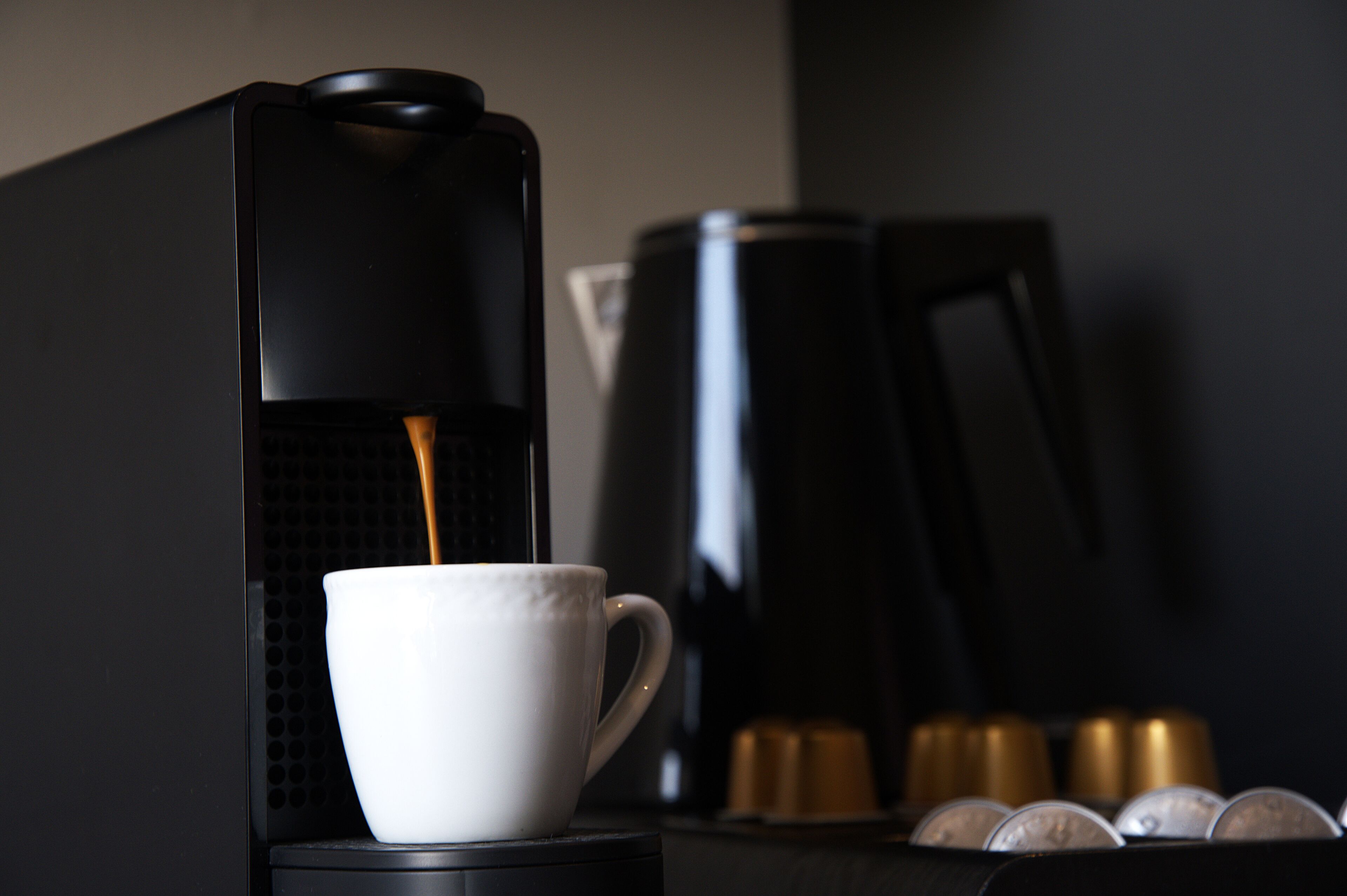 Máquina de café a servir café numa chávena, com uma pilha de cápsulas de café ao fundo.