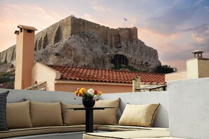 A terrace with a sofa and a table, a vase with flowers, and a view of a historic building with a flag. - CityZoe Athens Suites (Athens)