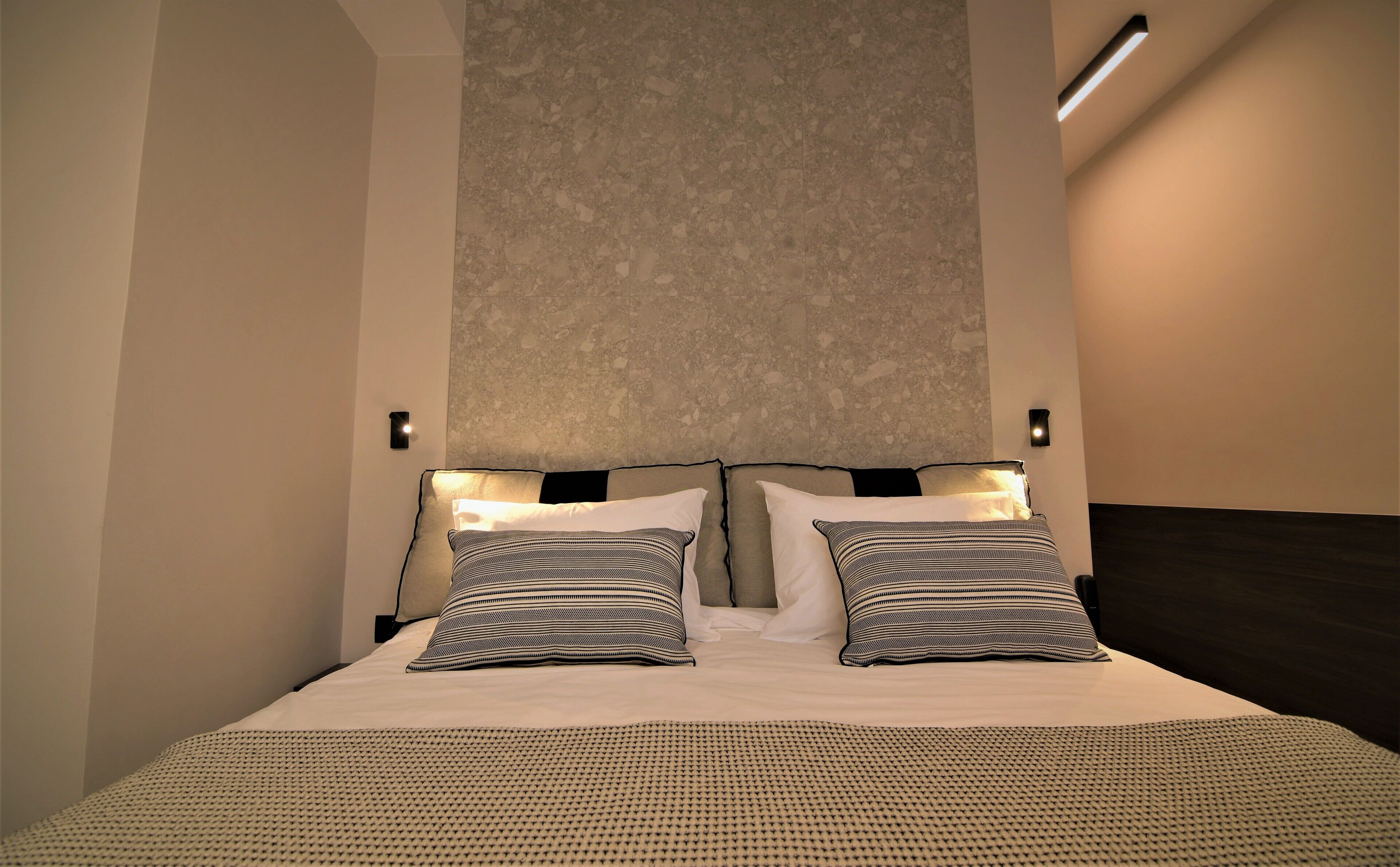A modern hotel room with a large bed, two bedside lamps, and a textured wall above the bed.