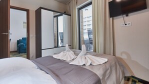 Ein Hotelzimmer mit Bett, Wandfernseher, Fenster mit Vorhängen und Spiegel, der den Raum reflektiert.