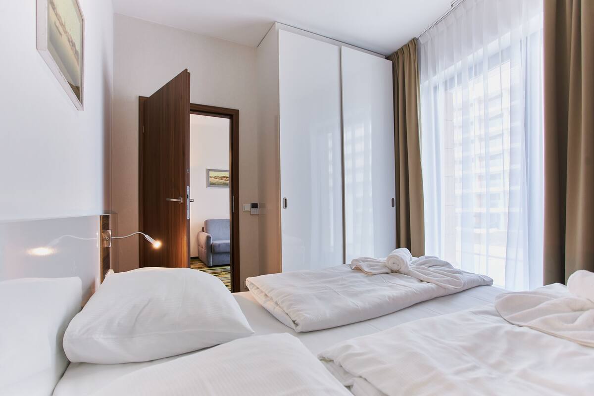 Ein Hotelzimmer mit zwei Betten, einem Schrank, einer Tür zu einem anderen Raum und einem Fenster mit Vorhängen.