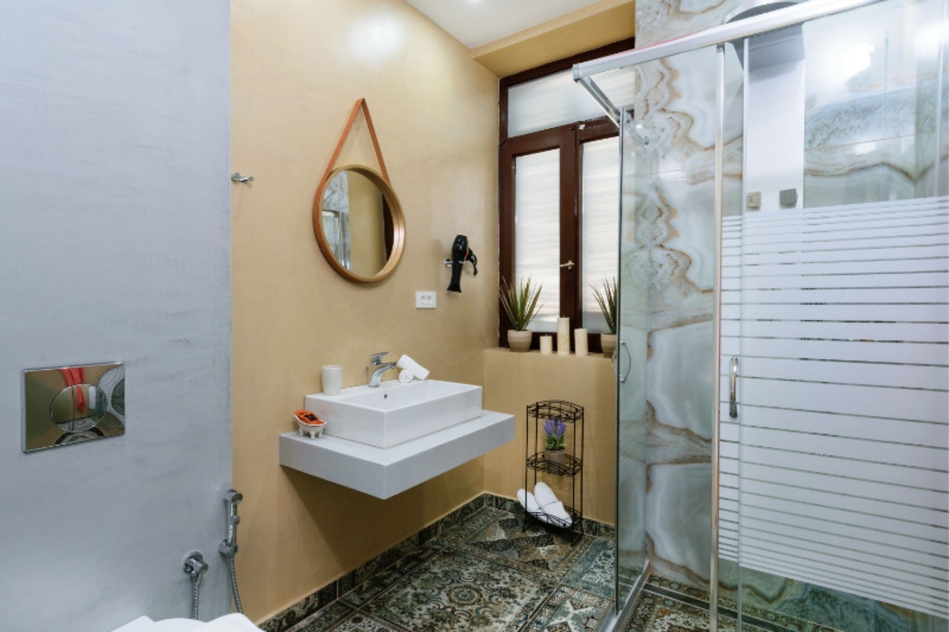 Un baño con lavabo blanco, espejo, ducha y piso estampado.